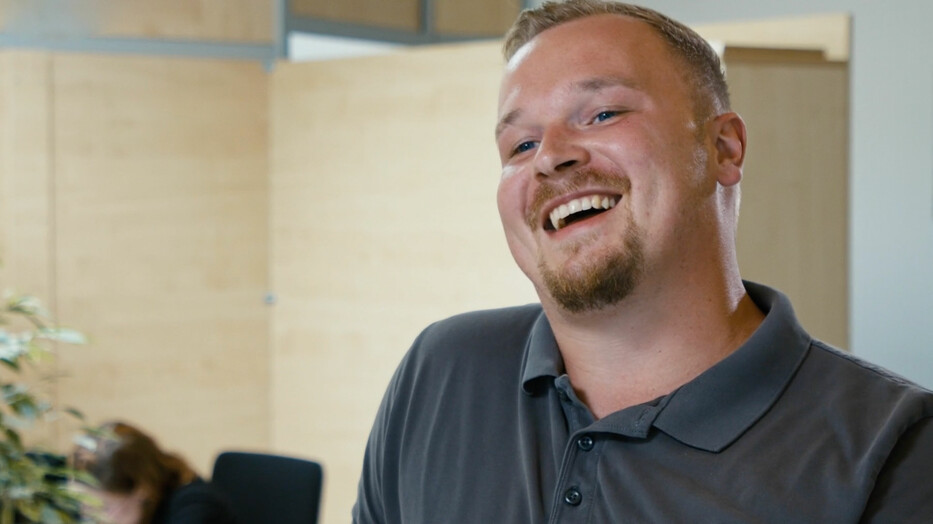 Vorschaubild zu Kurzinterviews. Kevin lächelnd im Gespräch.
